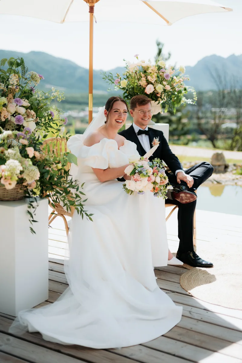 Mariés assis en terrasse avec bouquet, montagnes en fond
